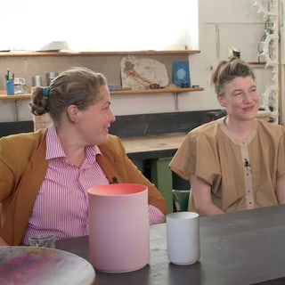 Zwei Personen sitzen in einem Kunststudio an einem Tisch.