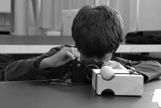Kind fotografiert mit Kamera im Raum sitzend.